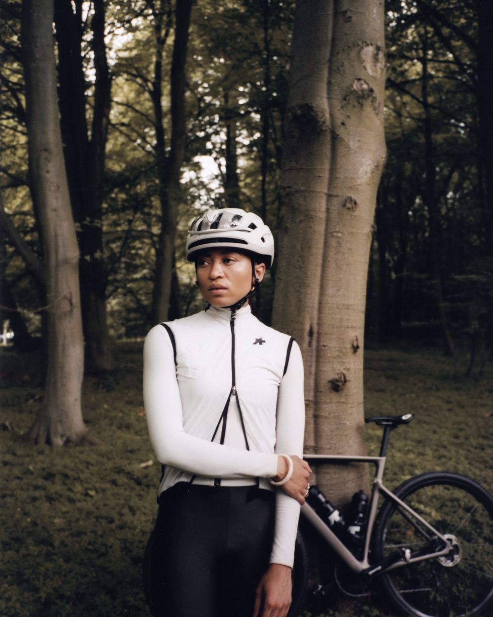 Rider in a white Assos winter layer standing with a bike in a forest