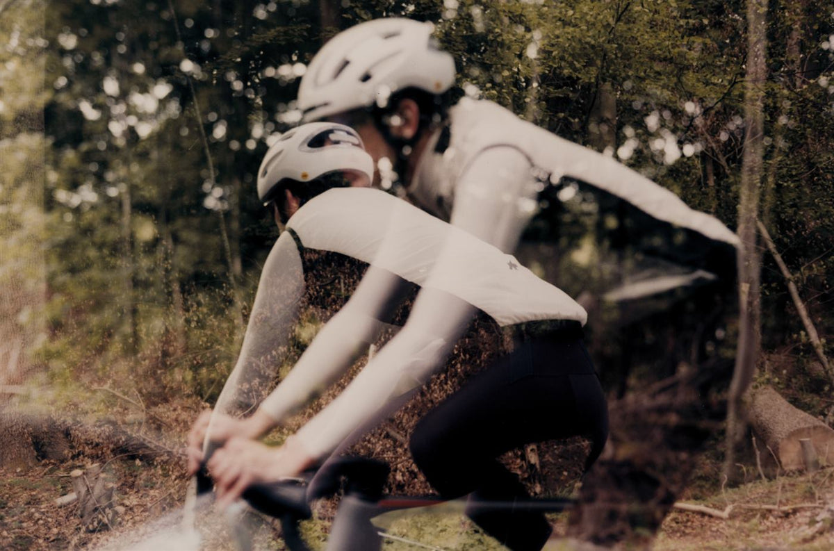 Two riders in Assos kit riding fast through a forest